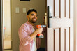 © AntonioDiaz - Smiling handyman installing a new door lock on a wooden front door using a power drill