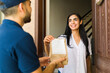© AntonioDiaz - Happy Latin young woman receiving a delivery of medication from a courier at her doorstep