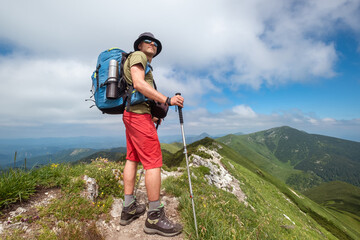 Wall Mural - hiker with trekking poles, backpack navigates rocky mountain trail on sunny day scenic background fe