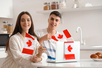 Canvas Print - Young couple with flags of Canada and laptop at table in kitchen