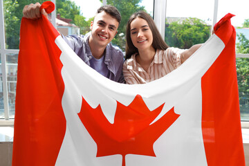 Canvas Print - Young couple with flag of Canada near window indoors