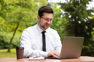 Canvas Print - Businessman working with laptop at table outdoors. Remote job