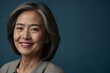 © Cristian - Asian woman with smile on her face next to empty space on dark blue background. Beautiful mature woman in stylish clothes in a studio with place for advertising text.