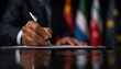 © narak0rn - Formal hand signing a document with international flags in the background, representing diplomacy and international agreements.