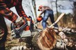 © alisaaa - Man with chainsaw cutting wood Two men, lumberjack using chainsaw for cutting wood outdoors, his colleague is holding the log