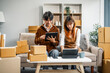 © NanSan - A young couple works from home, packing orders and managing their online store. They use technology and teamwork to run their business, smiling while fulfilling customer orders.