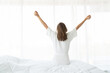 © janonkas - Woman stretching in bed after wake up. she sitting near the big white window while stretching on bed after waking up with sunrise at morning