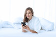 © janonkas - woman using Smartphone on bed to check Social media and morning news while wake up