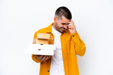 Wall Mural - Young caucasian man holding pizzas and burgers isolated on background laughing