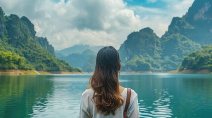 Canvas Print - Woman Looking At Lake. Rear view of Asian adult explorer admiring beautiful greenery mountains and blue lake