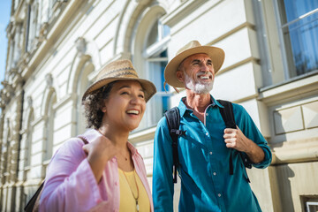 Poster - Elderly married couple exploring new city. They are wearing hats and backpacks.