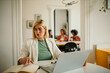 © La Famiglia - Successful businesswoman using a laptop and checking paperwork working in an office. Business technology corporate concept