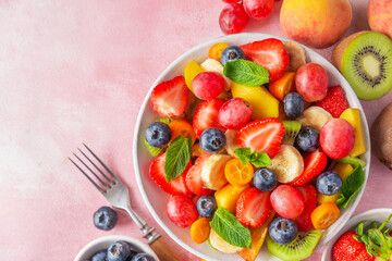 Poster - Summer fresh fruit salad in a bowl with fork on pink background. Top view. Healthy food for breakfast. Mixed strawberries, grapes, banana, kiwi, blueberries, peach, kumquat and mint for diet lunch