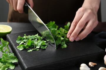 Woman cutting fresh coriander at black wooden table, closeup