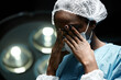 © Seventyfour - Dramatic portrait of young Black woman as tired female surgeon rubbing eyes in operating room copy space