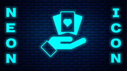 Canvas Print - Glowing neon Hand holding playing cards icon isolated on brick wall background. Casino game design. Vector