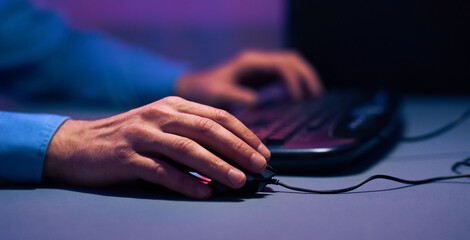 Poster - The image shows a closeup of a hand using a computer mouse. The person is sitting in front of a laptop, and the only light in the room is coming from the screen, cropped