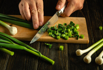 Wall Mural - A chef cuts green garlic on a cutting board with a knife to prepare a vegetable dish for lunch.