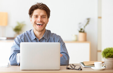 Aufkleber - A man sits at his desk with a laptop, smiling brightly and looking at the camera.