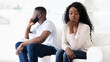 © Prostock-studio - A couple sits on a white couch, facing away from each other, seemingly in disagreement.