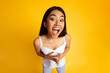 © Prostock-studio - A young Asian woman with long dark hair is wearing a white tank top. She is smiling with her mouth open wide, looking directly at the camera, high angle view