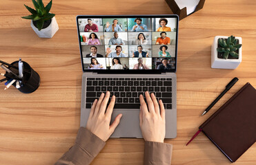 Poster - A person is participating in a video conference using a laptop computer. The screen shows multiple people in a grid format. The persons hands are on the keyboard of the laptop, top view