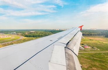 View of airplane wing, blue skies and green land during landing. Airplane window view.