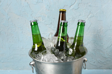 Bucket with bottles of cold beer and ice cubes on blue background