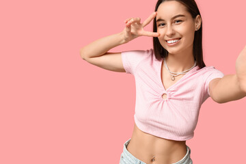 Wall Mural - Beautiful young happy woman with piercing navel taking selfie on pink background