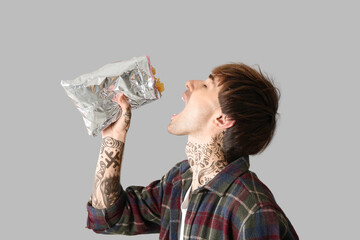 Sticker - Young tattooed man eating potato chips on light background