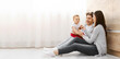 © Prostock-studio - A young family, consisting of a mother, father, and toddler, sit together on the floor of a modern home. The parents are smiling at their child, who is sitting on the fathers lap, copy space