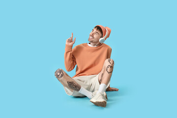 Wall Mural - Young tattooed man in headphones pointing at something on blue background