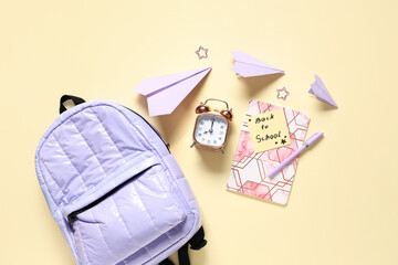 Wall Mural - Alarm clock, notebook, school backpack, paper airplanes, pen and paper clips on beige background