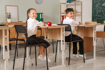 Sticker - Little schoolchildren with apples sitting at desks in classroom