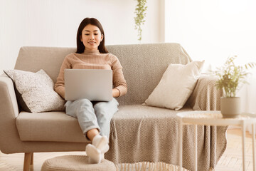 Poster - A woman sits comfortably on a beige sofa, using a laptop. Her legs are crossed and she is looking down at the screen. A plant and a side table are visible in the background.