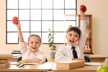 Wall Mural - Happy little schoolchildren with apples at desks in classroom