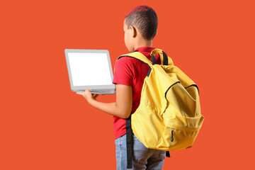 Wall Mural - Little schoolboy with laptop and backpack on orange background, back view