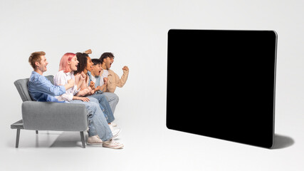 A group of four friends are sitting on a grey couch, watching television. The friends are excitedly watching the television screen, which is black and blank