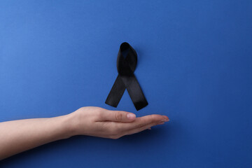 Wall Mural - Woman with black awareness ribbon on blue background, top view. Space for text