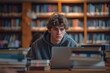 © Thodsapol - A young male student studies intently in a library, surrounded by books and a laptop, with a backdrop of bookshelves filled with knowledge