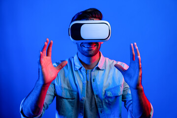 Wall Mural - Caucasian smart man holding and moving gesture while using VR goggle. Happy person using headset and goggle while enter virtual world or metaverse with neon light background. Technology. Deviation.