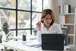 © crizzystudio - Young Asian businesswoman sitting at work using laptop and calculator document to calculate online finance, tax, accounting, statistics and analytical research concepts.