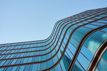 Modern building with curved glass facade reflecting sky. Contemporary architectural design against a clear blue backdrop