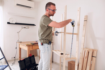 Wall Mural - Man assembling new wooden shelf and furniture in the apartment.