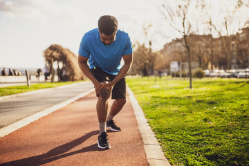 Young african-american man is injured while jogging. He has pain in his knee.