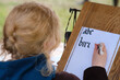 © Андрей Журавлев - A person with blonde hair is practicing calligraphy, writing the alphabet and the word 'bird' in black ink on white paper. They are using a calligraphy pen and a wooden writing board.
