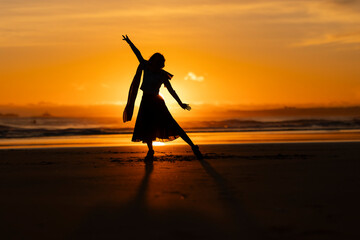 Wall Mural - A woman is dancing on the beach at sunset