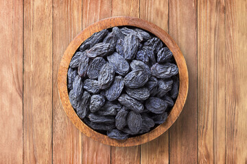 Wall Mural - blue raisins, dried grapes in bowl on wooden table background, top view. organic vegetarian food.