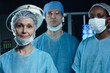 © Seventyfour - Waist up portrait of diverse medical team in operating room looking at camera with focus on mature woman surgeon in foreground, copy space
