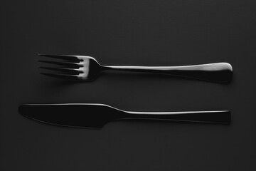 Poster - Close-up of two forks and one knife lying on a dark or black surface, possibly for food photography or still life